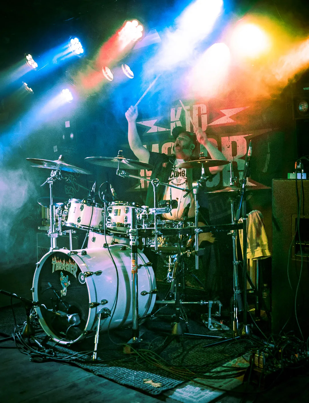 Chregu, Schlagzeuger von Kid Motor, live im bunten Scheinwerferlicht vor dem Kid-Motor-Backdrop
